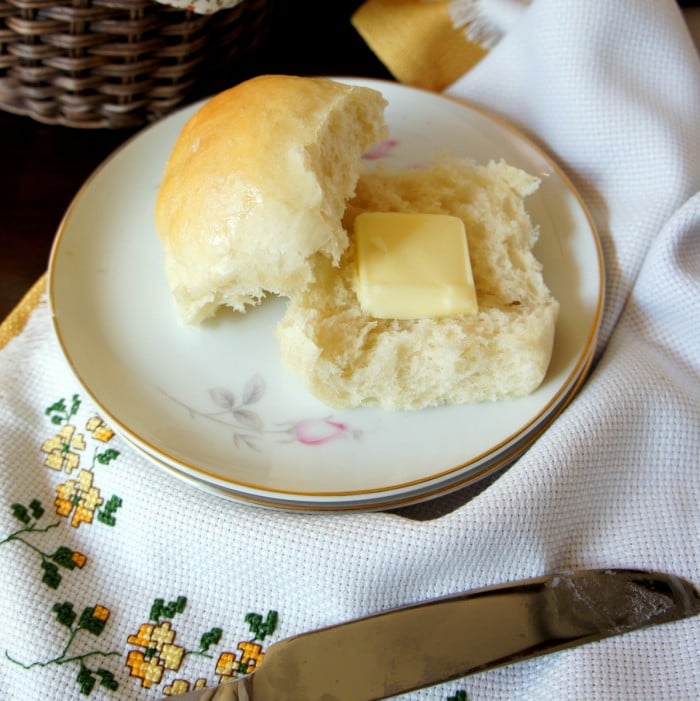 A baked roll sliced in half on a plate with a square of melting butter on one half