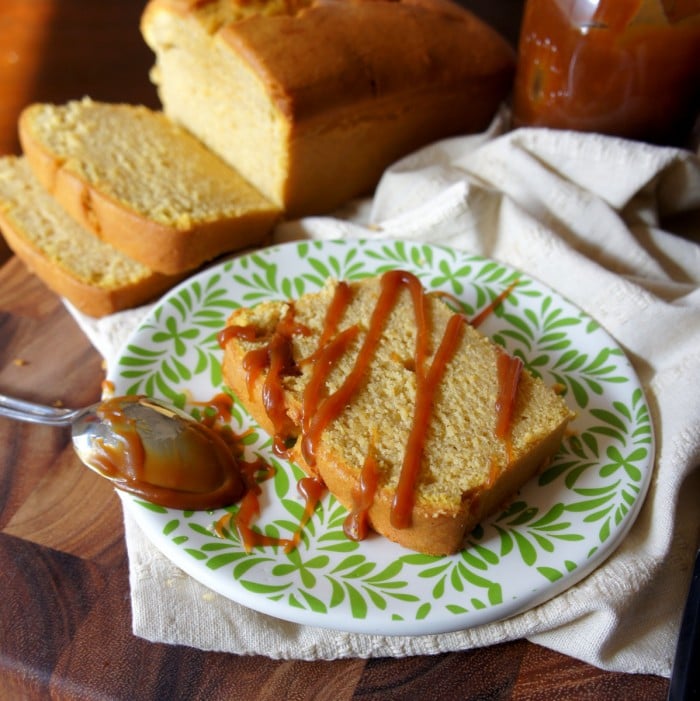 A display with a sliced pound cake and plate with a slice of pound cake on a plate with drizzled salted caramel on it