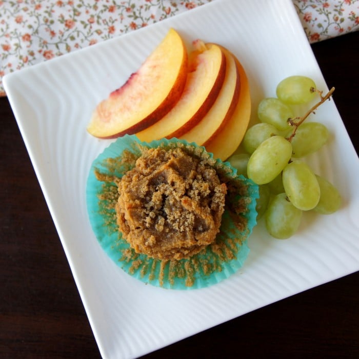 A plate with a Gluten Free Sweet Potato Muffin with a side of sliced peaches and a small bunch of grapes