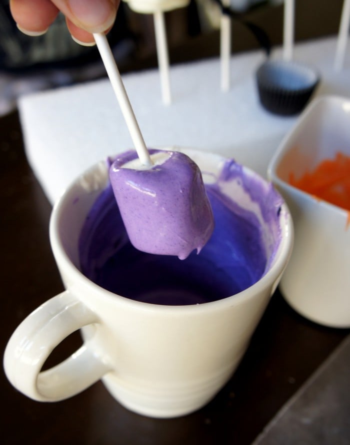 A marshmallow pop being dipped in purple colored white chocolate in a mug