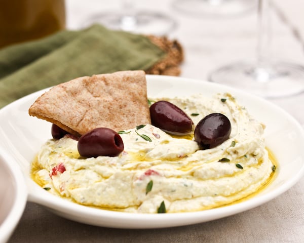 A triangle of pita bread dipped into a small bowl of his Spicy Feta Dip with Roasted Red Peppers