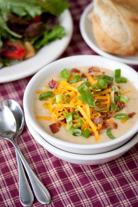 A bowl of soup with bacon, shredded cheese and chives on top