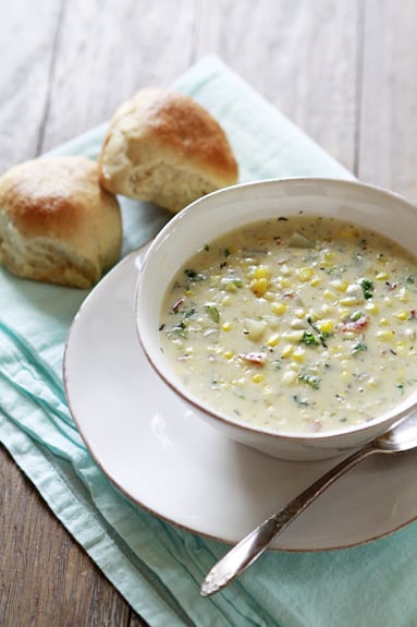 A bow of cream soup with vegetables and two rolls on the side