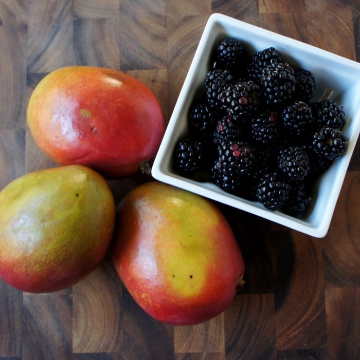 Three mangos next to a bowl of blackberries