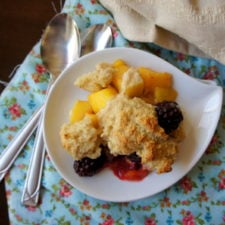 A plate with a scoop of cobbler on it with mango and blackberry