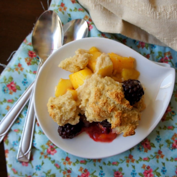 A plate of cobbler on a table, with blackberries and mango