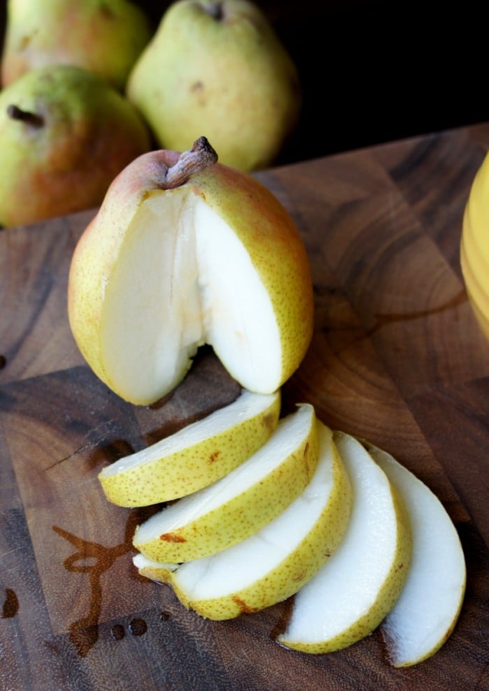 A slices of a pear displayed on a hard surface with a large pear next to it with a large slice removed