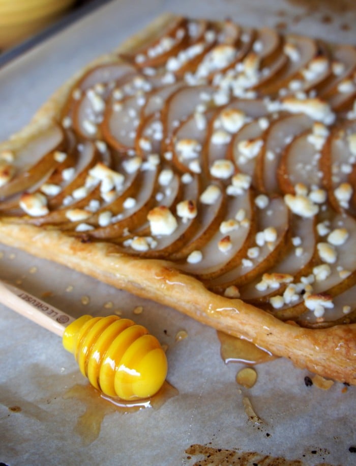 A close up of the crust of a pear tart with goat cheese and drizzled honey on top