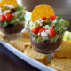 Five Layer Black Bean Dip in a glass cup over a tray of chips