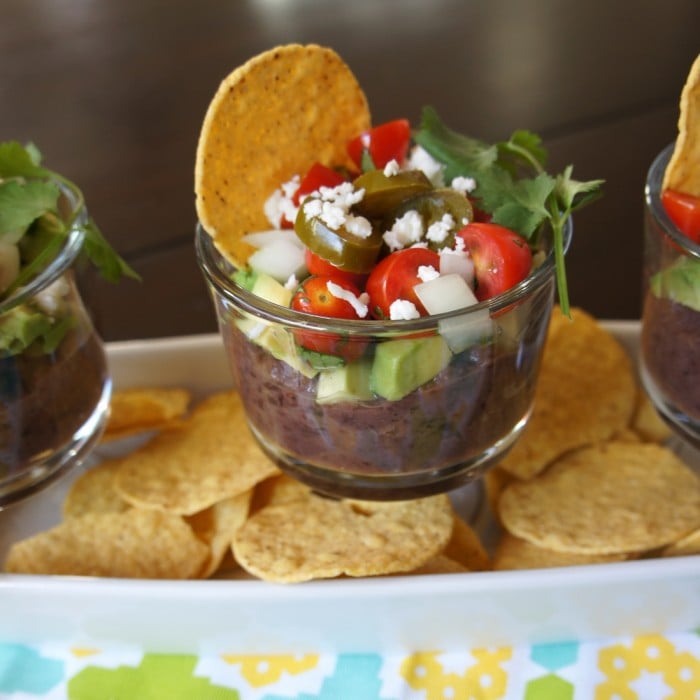 Bean dip in a small glass bowl with a chip surrounded by a pile of chips