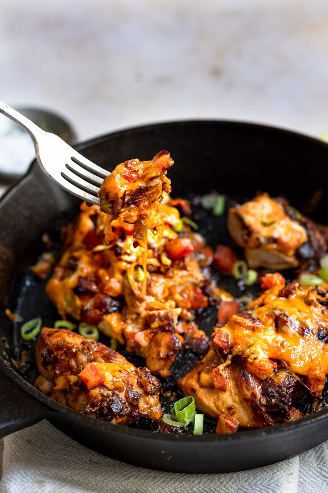 fork full of monterey chicken breast with bbq sauce, cheese and bacon. Topped with green onions.