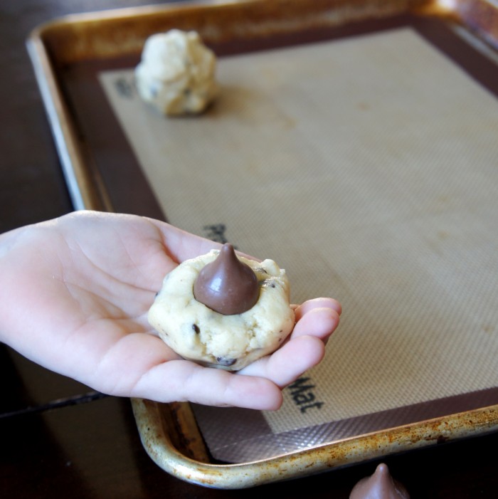 A hand holding a ball of raw cookies dough with a chocolate chip on top