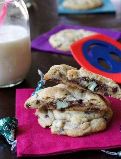 Mint Truffle Stuffed Chocolate Chip Cookies stacked on top of each other on a napkin next to a glass of milk