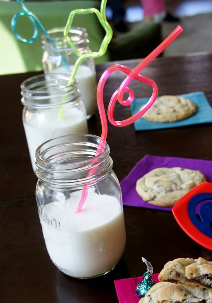 A display of cookies on a napkin next to glasses of milk with straws