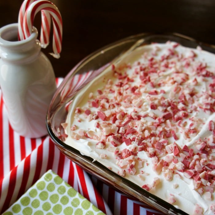 A close up of a glass baking dish with a white frosted cake topped in chopped peppermint chocolate pieces 