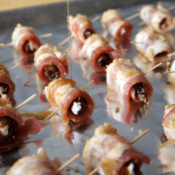 A close up of a baking pan with raw bacon wrapped dates