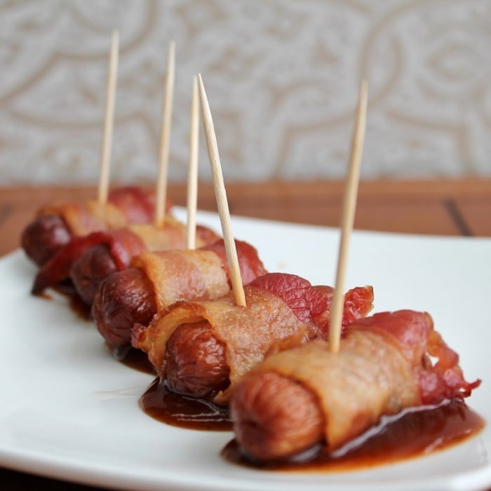 A plate with a line of bacon wrapped smokies with a toothpick in each