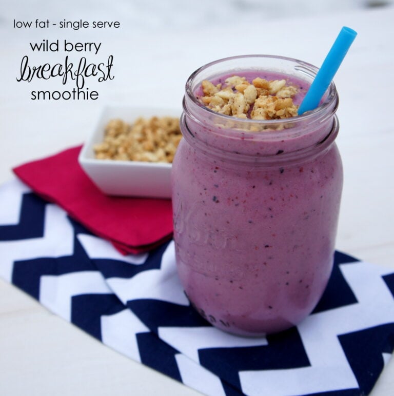A smoothie in a glass cup with granola on top and a blue straw next to a small bowl of granola