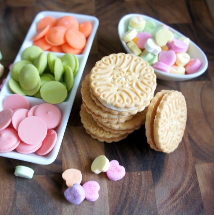 A display of pile of vanilla cookies with pink, green and orange chocolate melts and candied hearts