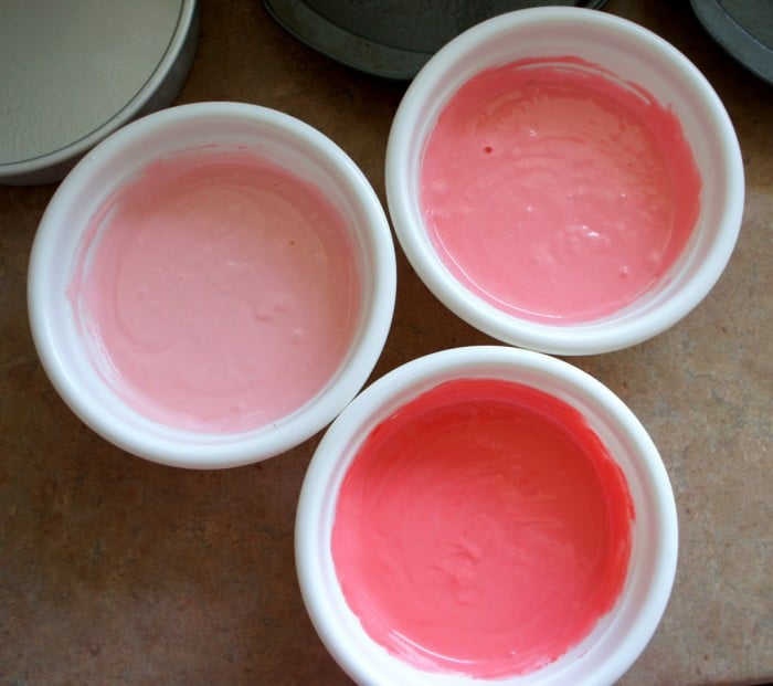 Three bowls of frosting in varying colors of pink 