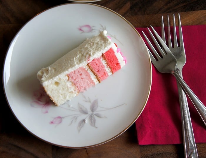 A slice of 4 layer ombre cake with white frosting on a plate