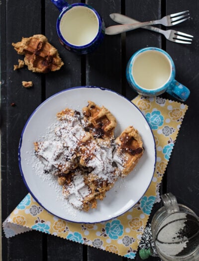 A plate of waffle cookies on a table next to a mug of milk