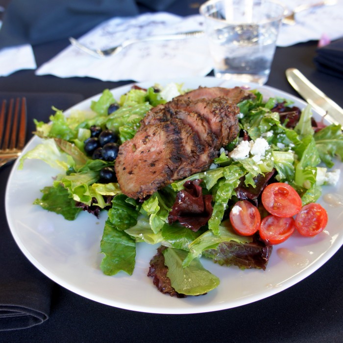 A plate with a white plate with sliced beef on a bed of lettuce and veggies