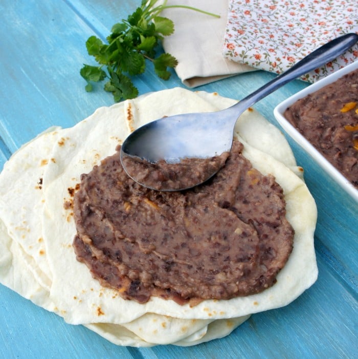 A spoon spreading refried beans on a tortilla 