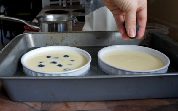 A hand adding blueberries to the filled ramekins