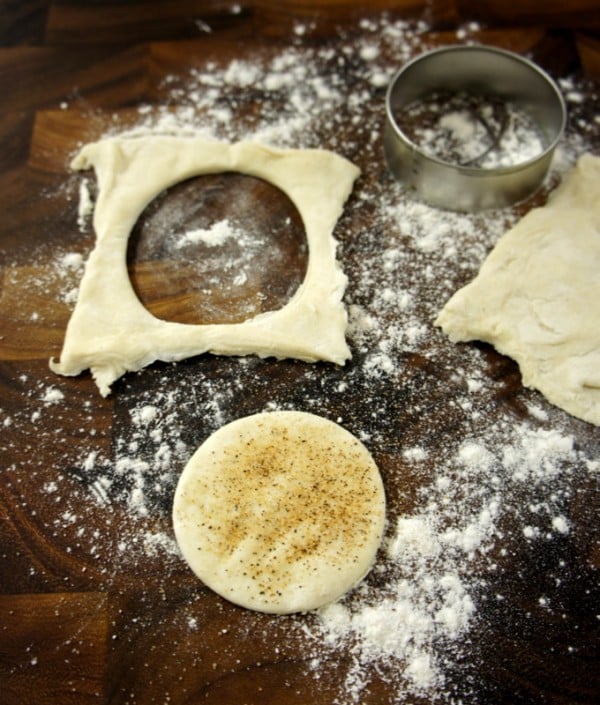 A wooden surface with raw dough circle cut out of a square of dough