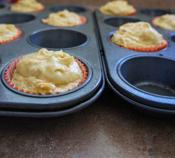 A close up of a muffin tin with cupcake liners overfilled with batter 