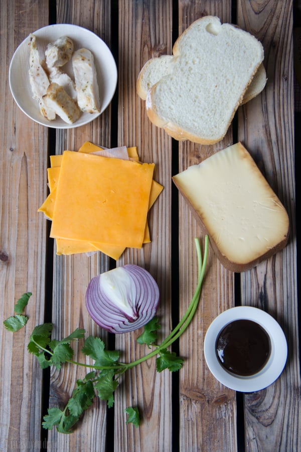 A display of ingredients needed to make BBQ Chicken Grilled Cheese Sandwich: chicken, bread, cheese slices, onion, BBQ sauce