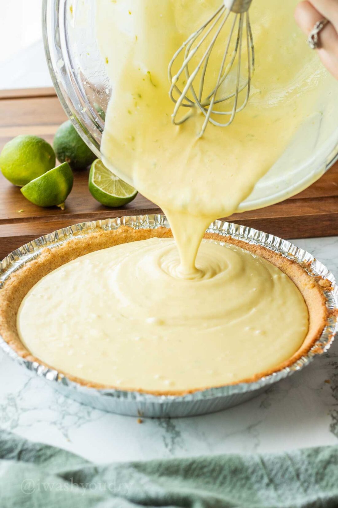 Pouring key lime pie filling into baked graham cracker pie shell. 