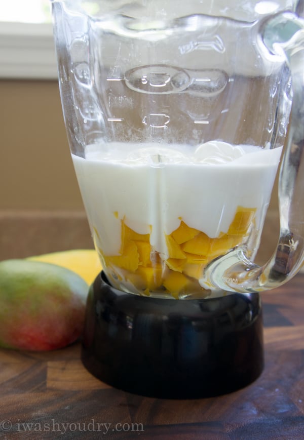 A close up of glass blender with mango and cream