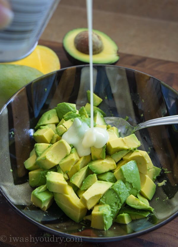 A close up of bowl of avocado chunks with a white liquid being poured on top