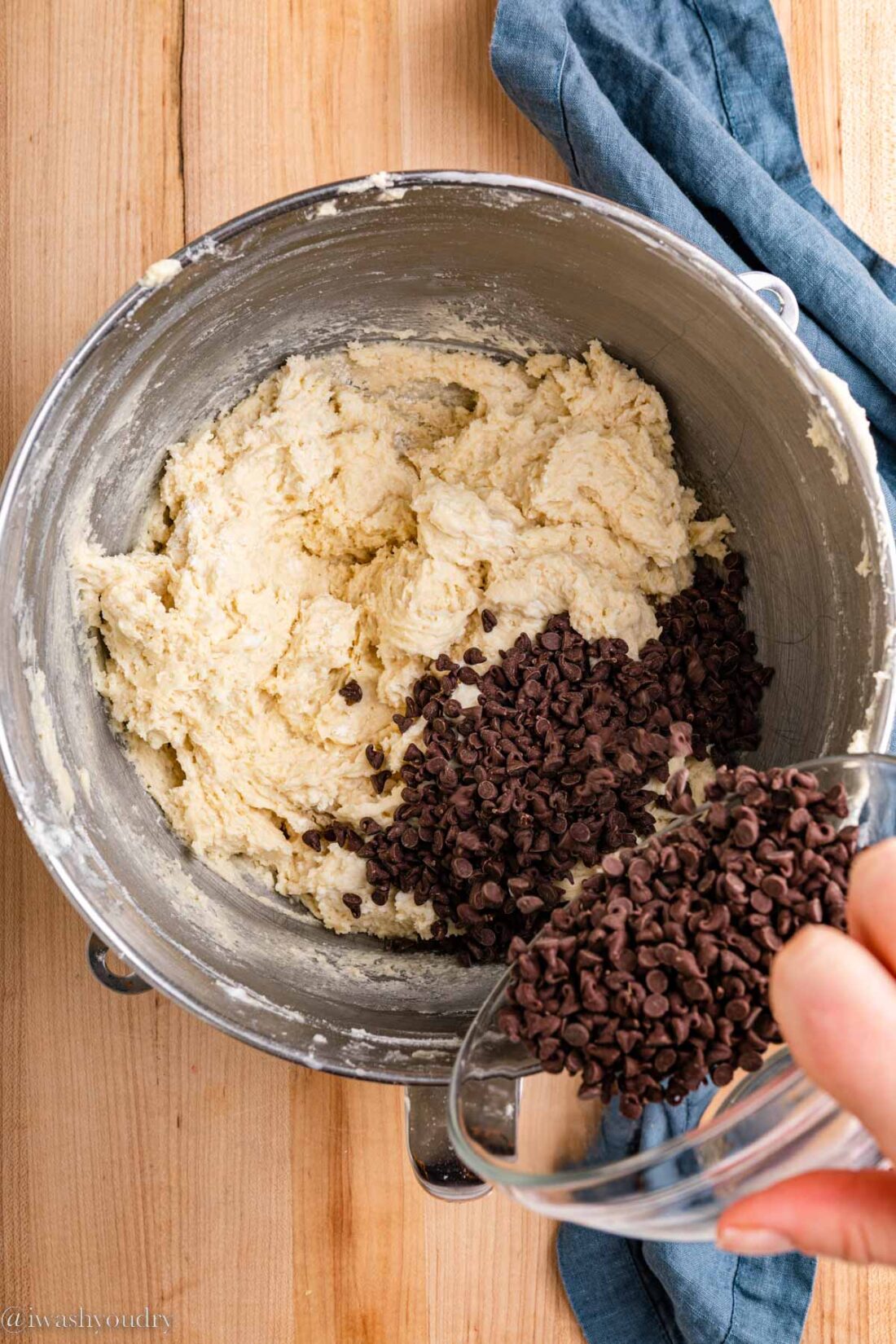 Hand pouring chocolate chips into muffin batter in metal mixing bowl,. 