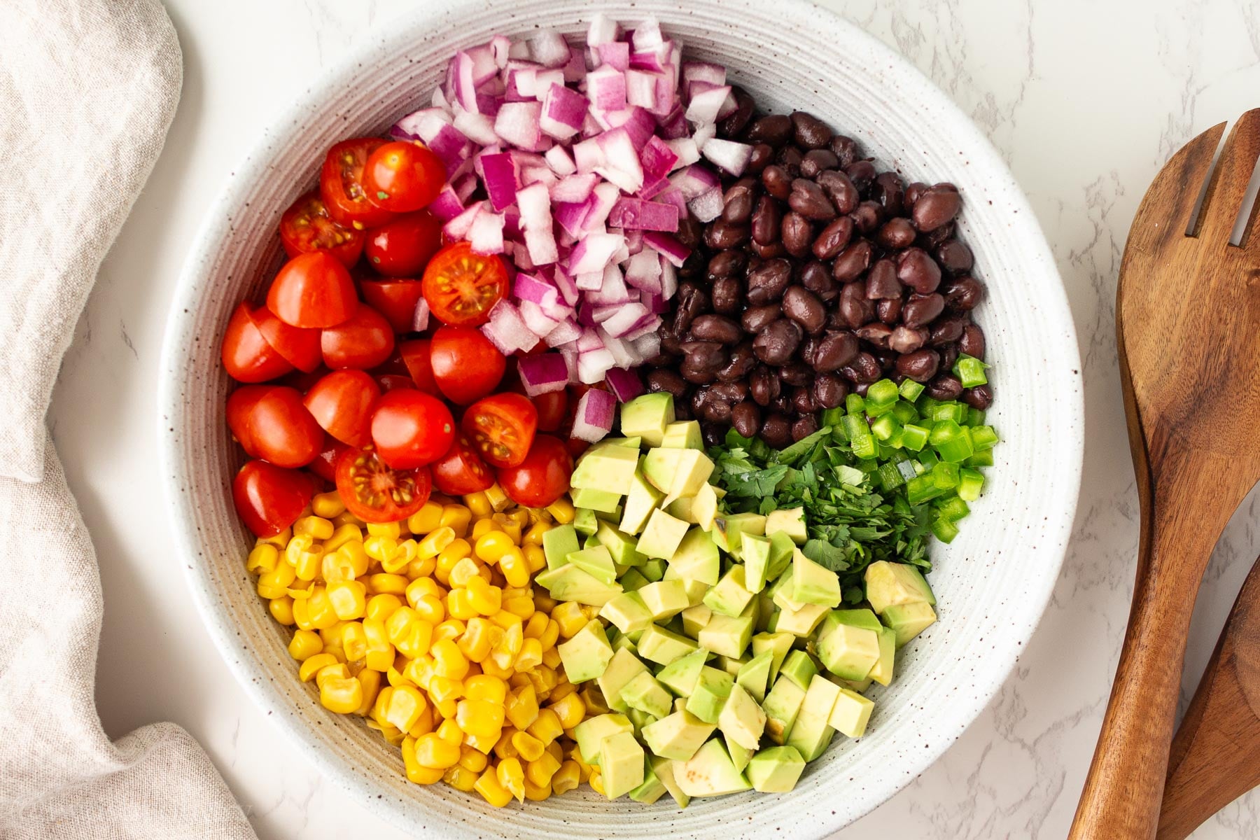 cowboy caviar with black beans and corn in white bowl with wooden spoon next to it.