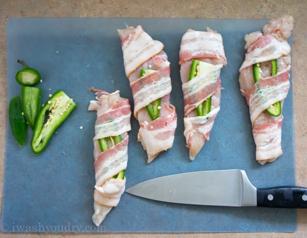A cutting board with raw chicken and a slice of Jalapeño wrapped with raw bacon