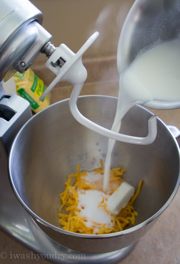 A close up of a mixing bowl filled with cheese and milk being poured into the bowl