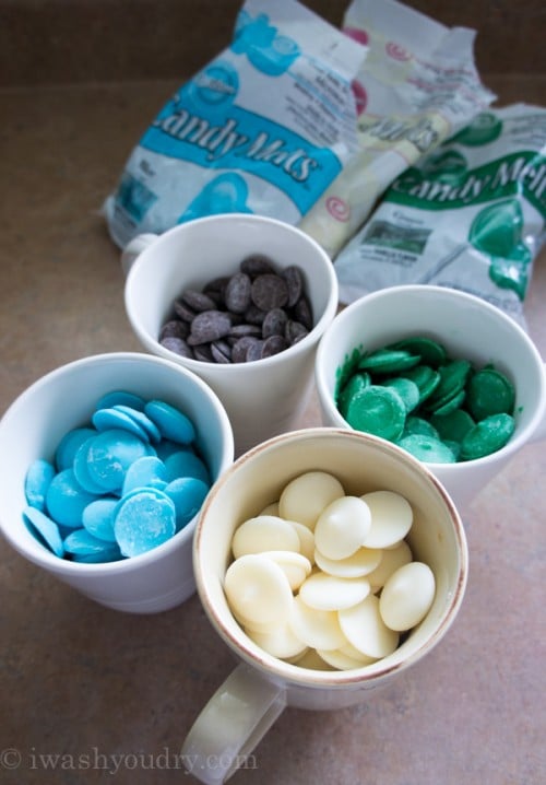 A close up of four bowls with colored chocolate melts of; blue, green, white and chocolate