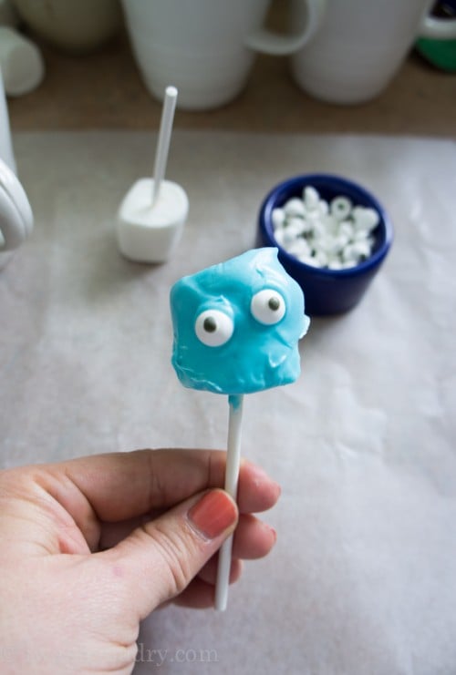 A close up of a blue frosted marshmallow pop with 2 candied eyes