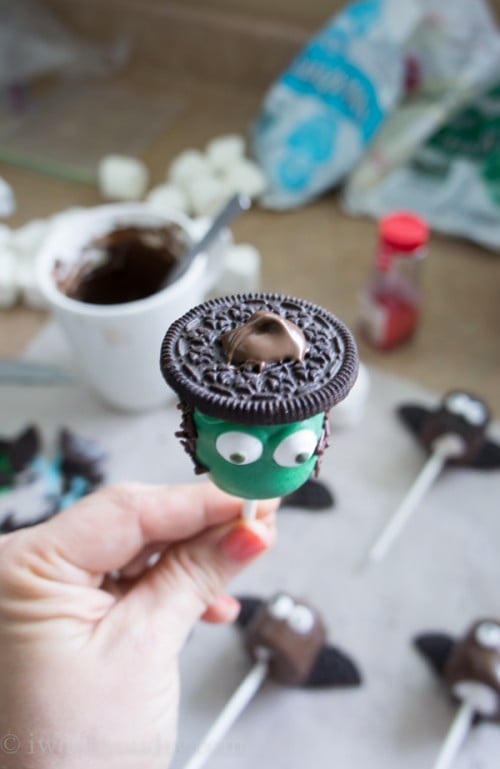 A close up of a green colored marshmallow pop with eyeballs topped with an Oreo cookie