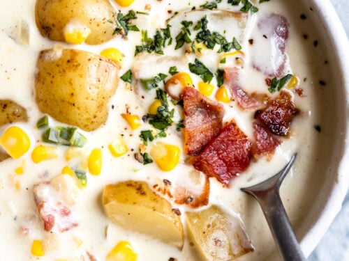 Spoon in bowl of chowder with potatoes and corn