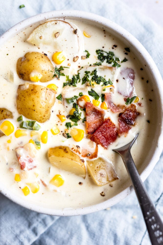 Spoon in bowl of chowder with potatoes and corn