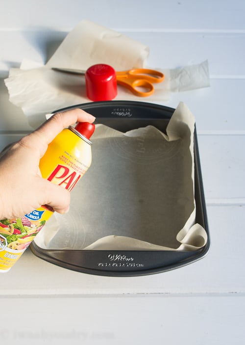 A baking pan lined with parchment paper being sprayed with Pam