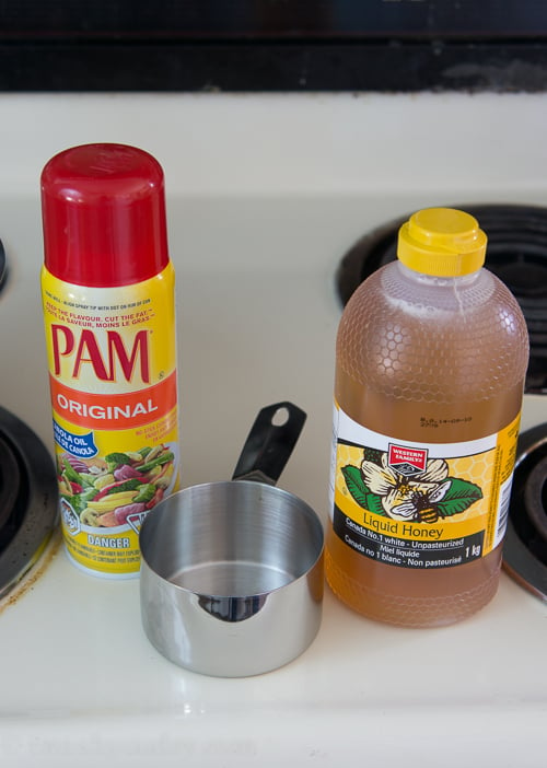 A bottle of Pam spray next to a measuring cup and a jar of honey