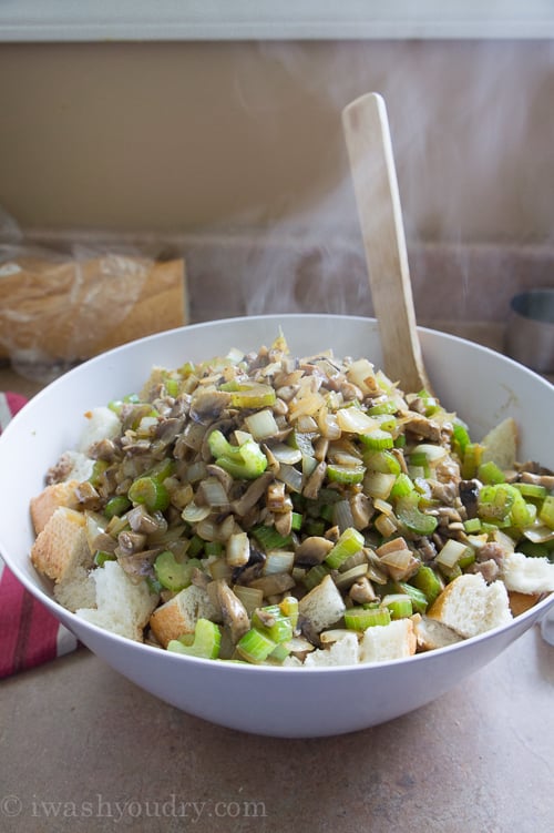 A bowl of steaming food on a table, with bread crumbs and veggies