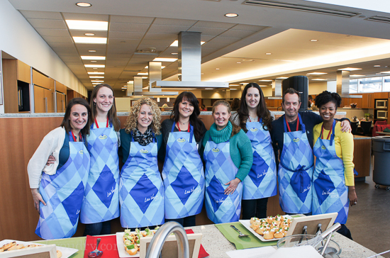 A group of people standing in a line with blue aprons behind a table of prepared food