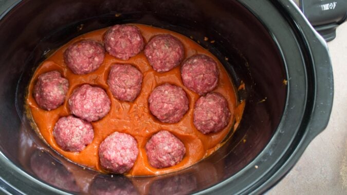 Uncooked meatballs in pasta sauce inside slow cooker