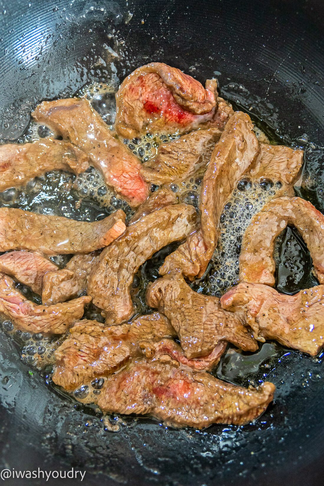 beef cooking in a skillet with oil.